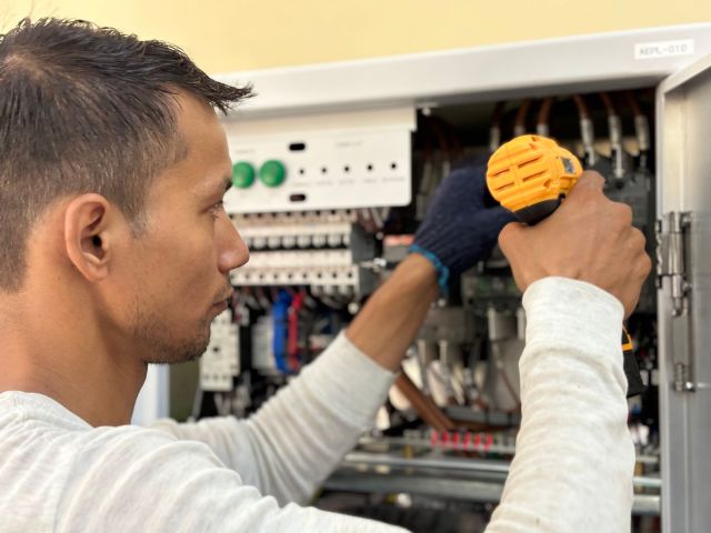 Technician repairing components inside an elevator control cabinet