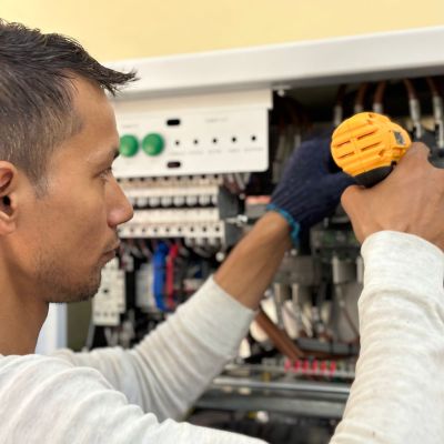 Technician repairing components inside an elevator control cabinet